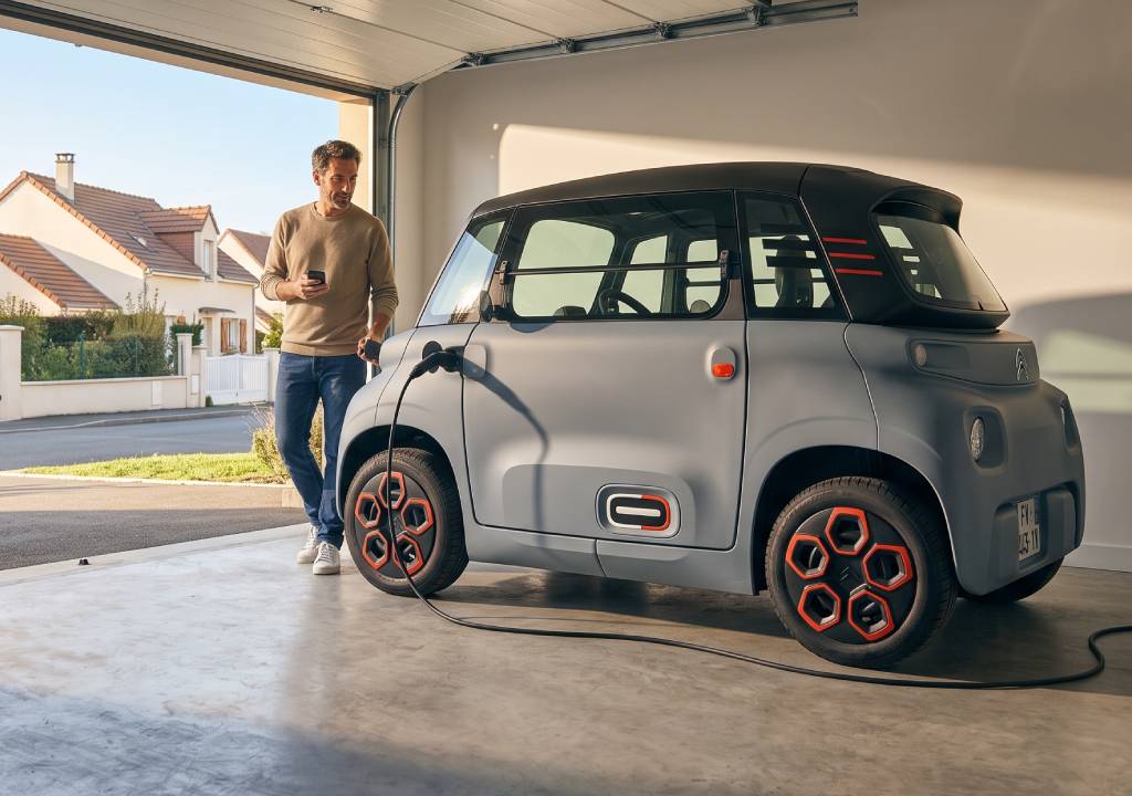 Homme dans las trentaine dans son garage qui attends que sa voiture ami se recharge